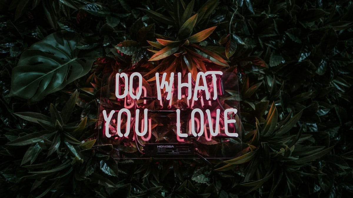 A neon sign reading "DO WHAT YOU LOVE" mounted on a wall of green leaves
